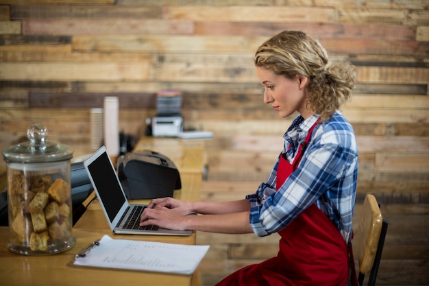 Waitress sitting at counter and using laptop in coffee