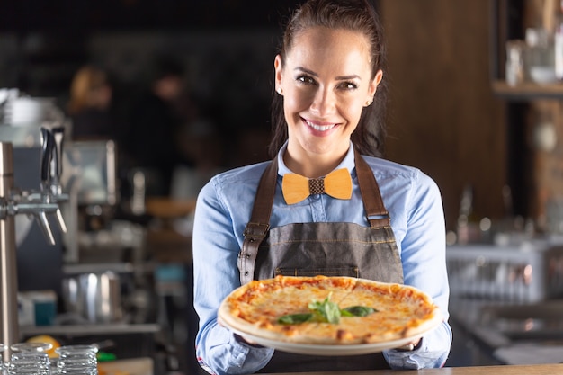 Waitress smiles while serving large authentic Italian pizza in a restaurant.