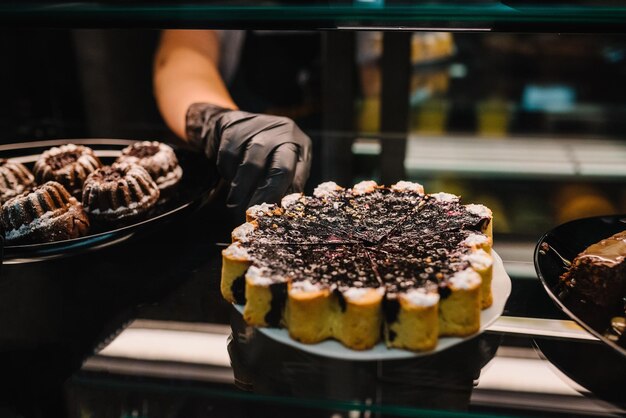 The waitress takes the cake on a glass display at the coffee shop Female hands offering fresh pastry in a sweets shop