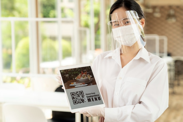 Waitress with face shield and face mask showing the menu