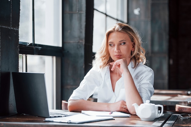 Waits when file will open. Businesswoman with curly blonde hair indoors in cafe at daytime.