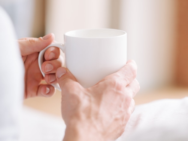 Wake up beverage. Man hands with white cup of hot morning drink. Close up.