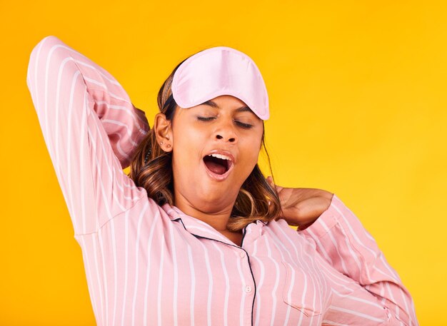 Wake up yawn and a woman on a yellow background in pyjamas for sleeping tired and in the morning fatigue young and a girl or person in clothes for rest comfort and a nap in a studio for night