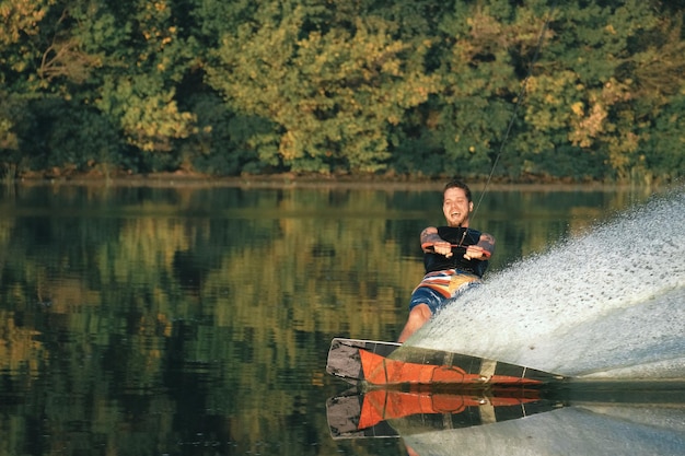 Wakeboarden, man wakeboarder glijdt op water met wakeboard en creëert spatten, groene achtergrond