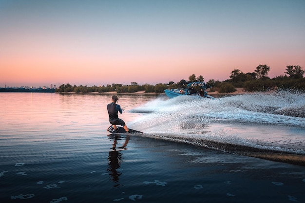 Wakeboarden, wakeboarder glijdt over water met wakeboard creëert spatten achter de boot, zonsopgang