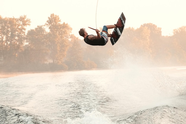 Wakeboarding, man wakeboarder does the trick backflip on the river. morning time