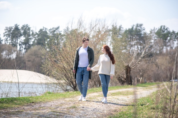 Walk in nature. Delighted attentive man looking at pretty woman holding hands walking in nature on sunny spring day