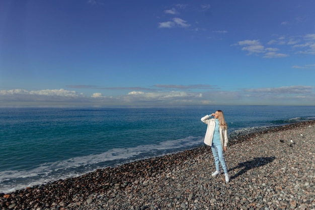 寒い季節に海岸を歩く暖かい服を着た女性が海の地平線を越えて見える