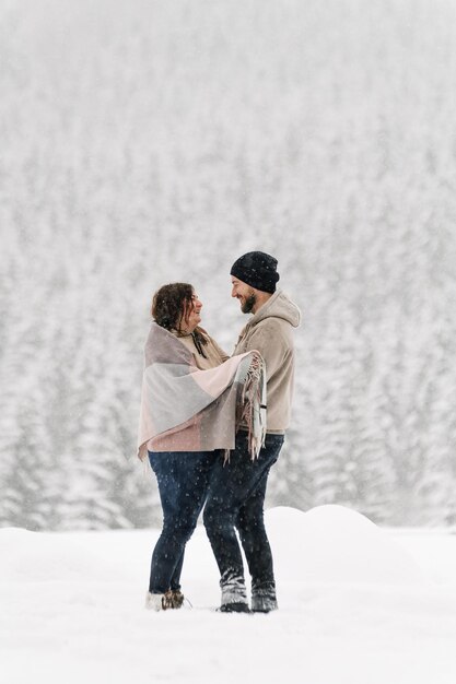 Walk in winter. Embracing couple enjoying snowfall. Man and woman having fun in the frosty forest. Romantic date in winter time.Christmas mood of a young family. Love and leisure concept