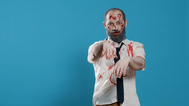 Photo walking dead corpse with deep and bloody wounds standing on blue background. horror looking brain-eating crazy monster acting bizarre while growling sinister at camera. studio shot