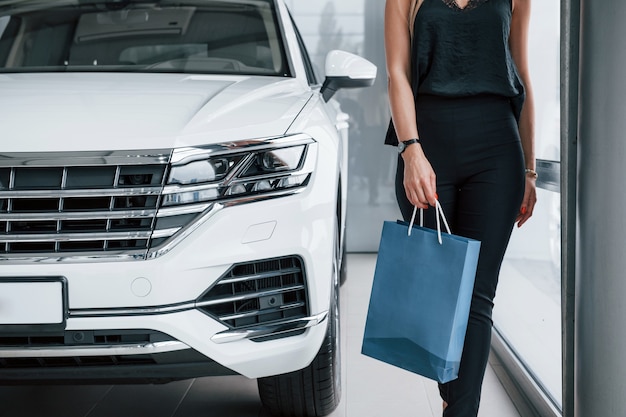 Walking forward. Girl and modern car in the salon. At daytime indoors. Buying new vehicle.