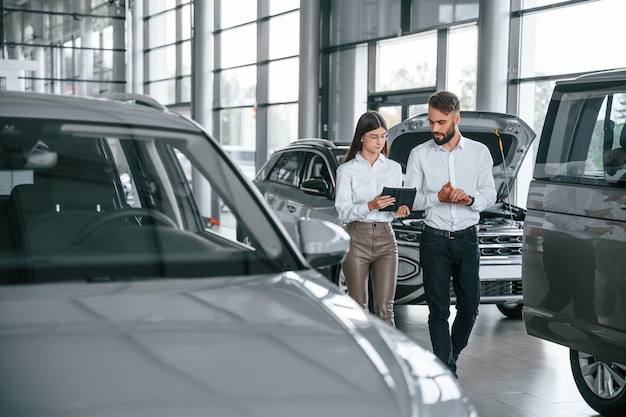 前に歩いて話している白い服を着た女性と男性が一緒に自動車ディーラーにいる