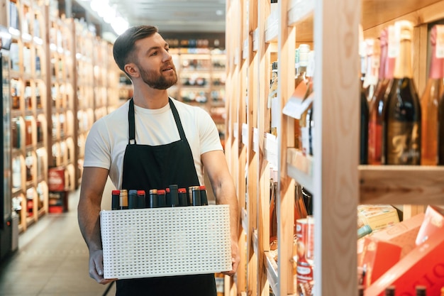 Photo walking and holding bunch of bottles wine shop owner in white shirt and black apron