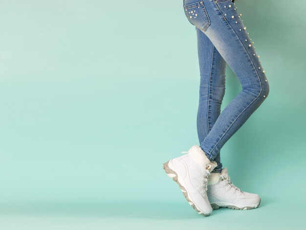 Walking legs of a girl in tight jeans on blue. Winter sports style.