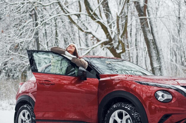 Walking out off car Beautiful young woman is outdoors near her red automobile at winter time