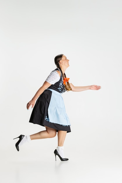 Walking. Portrait of beautiful woman, waitress in traditional Austrian or Bavarian costume standing alone isolated over white background. Holiday event, celebration, oktoberfest, festival concept.