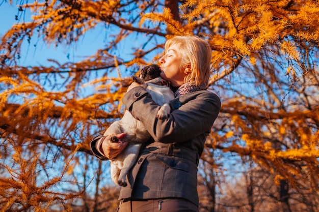 Cane ambulante del carlino nella sosta di autunno. donna felice che abbraccia e bacia l'animale domestico.