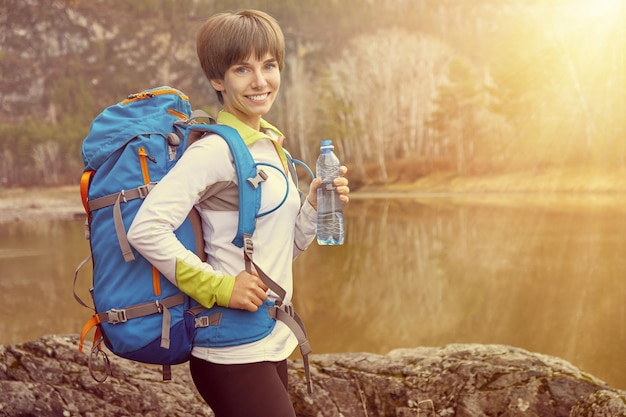 水のボトルとバックパックで笑顔の若い女性を歩く屋外スポーツの肖像画