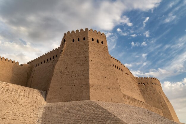 Wall of IchanKala old city with KunyaArk citadel at sunset against light clouds Khiva Uzbekistan