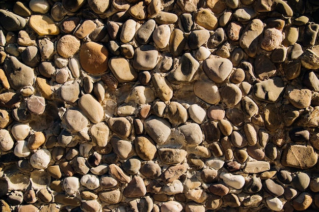 The wall is grayAbstract backgroundThe texture of a stone wall A stone wall made of round cobblestones Sunlight falls on the wall