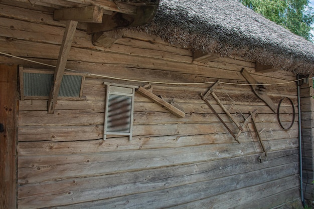 Wall of a log village hut with hand tools for farming