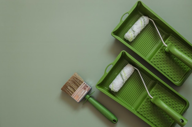 Wall paint roller and brush on green background top view