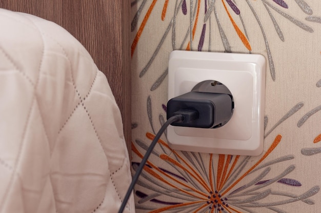 Wall socket with charger plug inside close to bed on paper wall