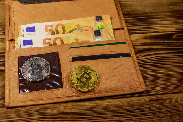 Wallet with fifty euro bills and bitcoins on wooden background