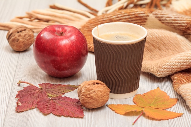 Walnoot, kopje koffie, appel, geruite plaid en droge bladeren op houten planken. Een herfststilleven.