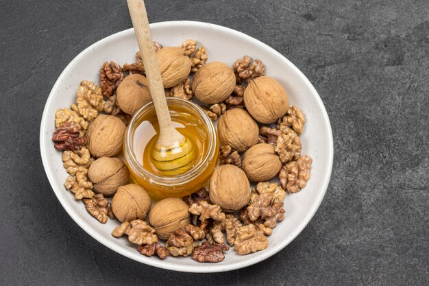 Walnut kernels, whole walnuts, nuts, glass jar with honey in white ceramic bowl