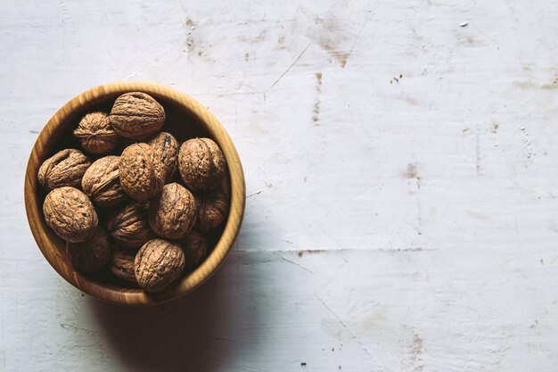 Walnut kernels in a wooden bowl and whole walnuts on a table. Walnuts