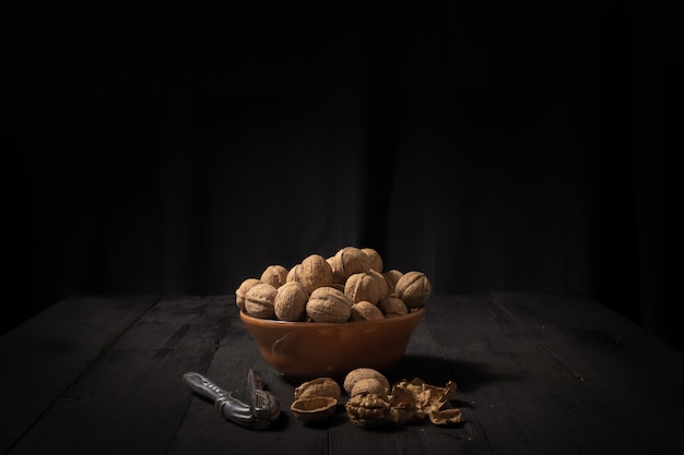 Walnuts in a bowl on dark surface. Low-key image of nuts on black rustic table, artistic light and shadow technique and copy space