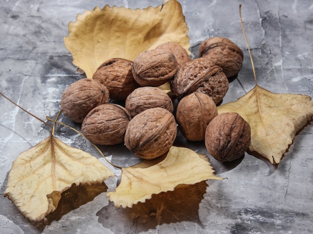 Walnuts and fallen autumn leaves on a gray concrete table