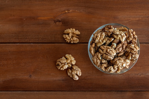 Walnuts in glass bowl on wooden table. Place for text, top view