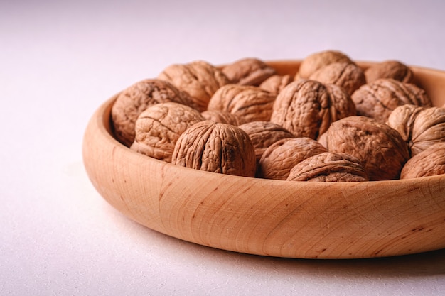 Walnuts heap food in wooden bowl on white background, angle view, healthy food concept