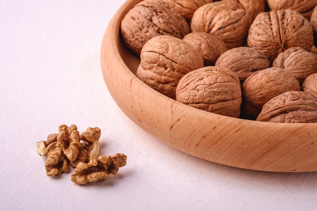 Walnuts heap food in wooden bowl on white background near to peeled nuts, angle view, healthy food concept