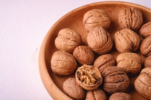 Walnuts heap food in wooden bowl on white background with half peeled nut, angle view, healthy food concept