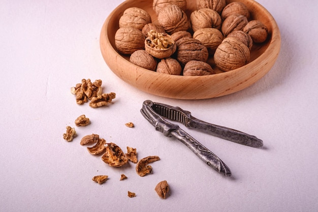 Walnuts heap food in wooden bowl with half peeled nut, cracked nutshell, near to vintage nutcracker on white background, angle view, healthy food concept