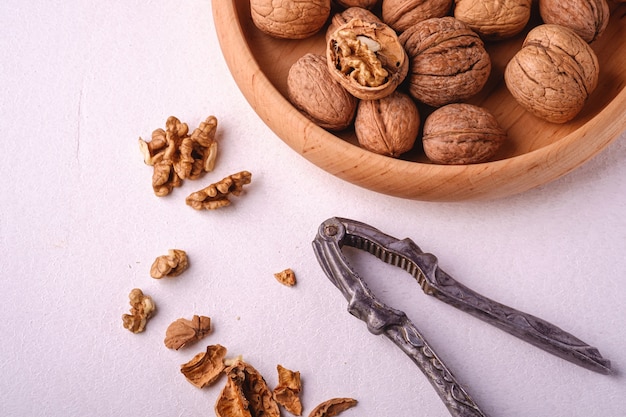 Walnuts heap food in wooden bowl with half peeled nut, cracked nutshell, near to vintage nutcracker on white background, angle view, healthy food concept