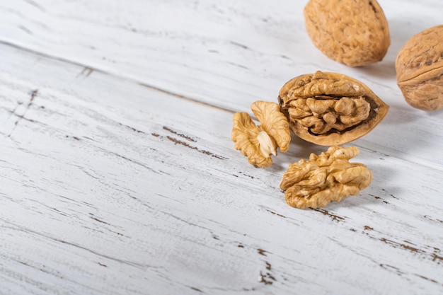 Walnuts kernels on white wooden desk with place for text. Top view of pile of whole walnut shells