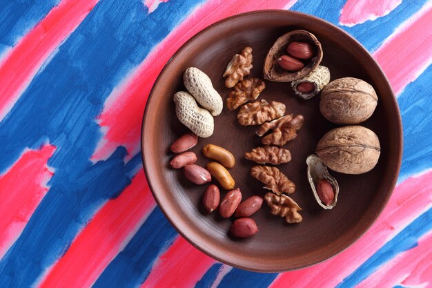 Walnuts and peanuts on a clay plate on a bluepink background vegan food peeled and unshelled nuts on a pink and blue background closeup