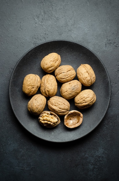 Walnuts in a plate on a dark concrete background. Nuts are a source of vegetable protein and vitamins. Flat top view, copy space