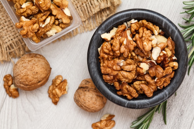 Walnuts in stone bowl and plastic container on a wooden background.