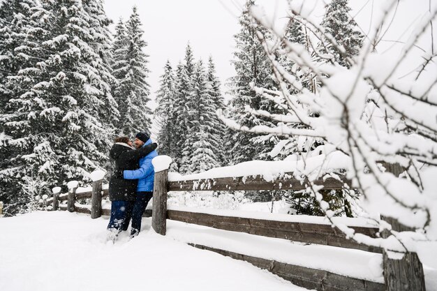 Wandel in de winter. Omhelzend paar die van sneeuwval genieten. Man en vrouw hebben plezier in het ijzige bos. Romantische datum in de winter. Kerststemming van een jong gezin. Liefde en vrije tijd concept