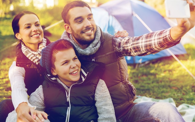 wandel-, reis- en technologieconcept - gelukkig gezin met smartphone die een selfie maakt op de camping