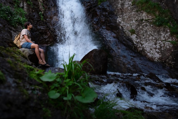 Wandelaar waalkinh met rugzak kijkend naar waterval in park in prachtig natuurlandschap