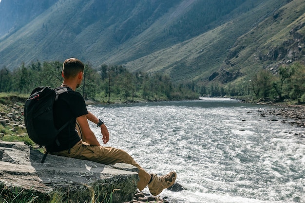 Wandelaar zittend op een steen aan de rivieroever tegen de achtergrond van berghellingen