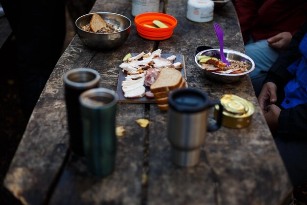 Wandelaarsontbijt houten tafel met brood, spekblikjes, andere maaltijden en warme mokken op het boskamp