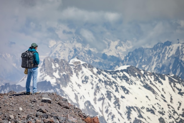 Wandelaarvrouw die opstaat en de top bereikt. Uitzicht op de besneeuwde bergen.