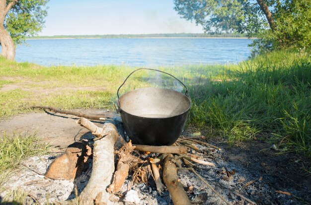 Wandeling naar de natuur. eten koken in een pot boven het vuur op een zonnige zomerdag. kampeereten aan de oever van het meer.